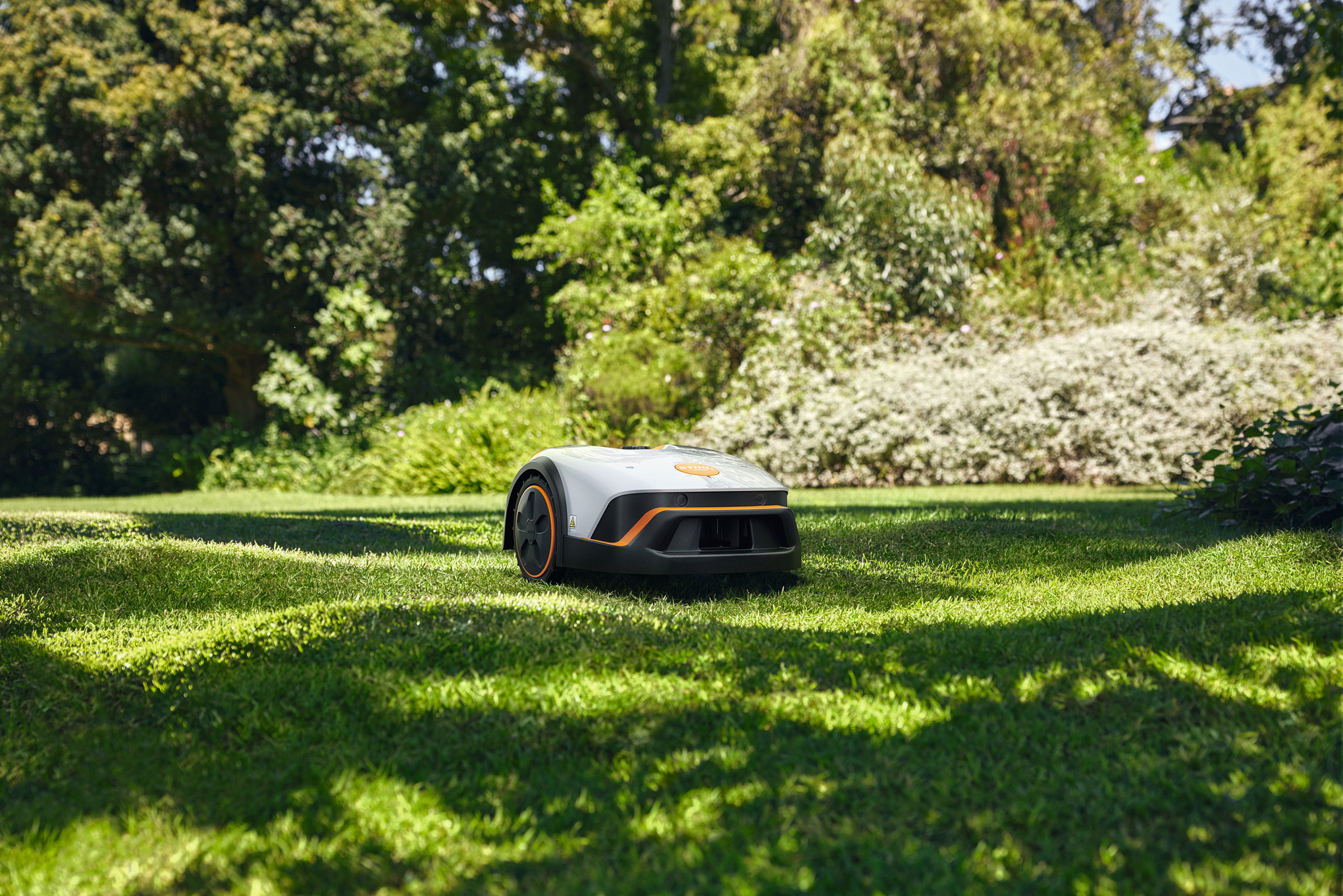 A STIHL iMOW® robot mower on mowing a sun dappled lawn
