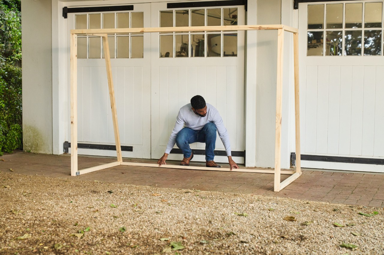 A man attaches the floor strut of the football goal to the back of the side wall