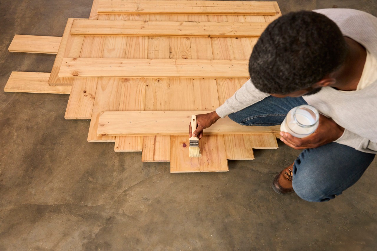 A man varnishes wooden floor base with wood protection oil