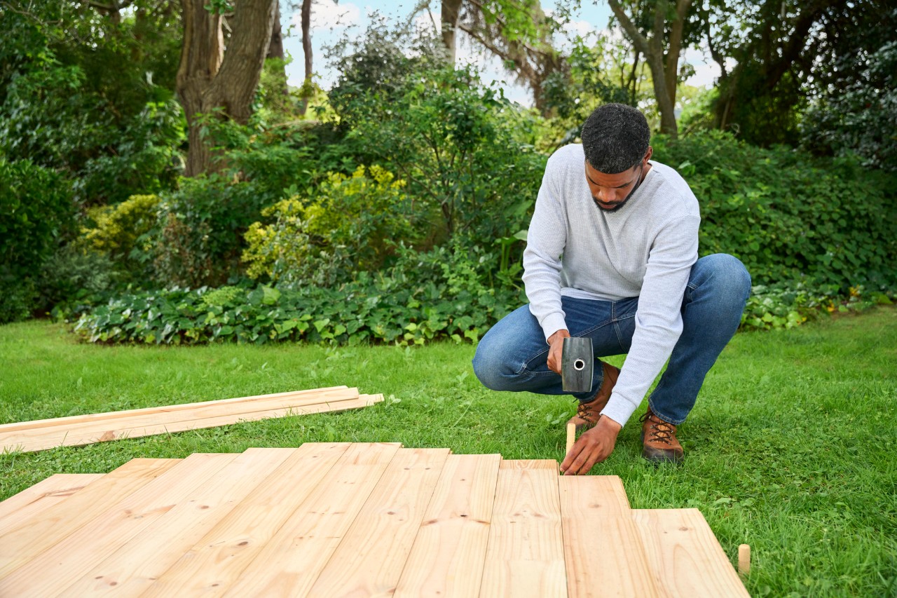 A man hammers wooden stakes around the base structure to mark where the tent poles need to go