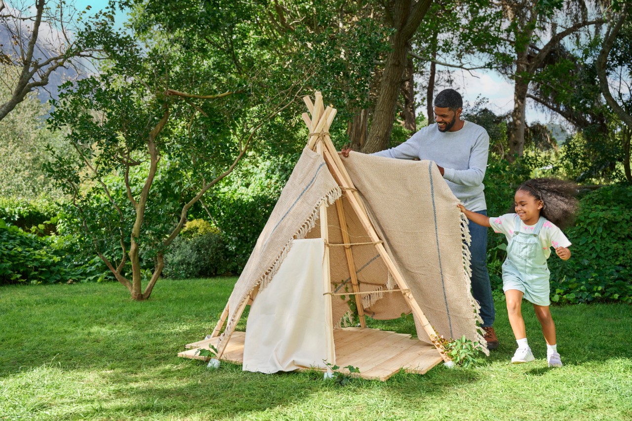 Man and little girl cover the tent structure with a blanket