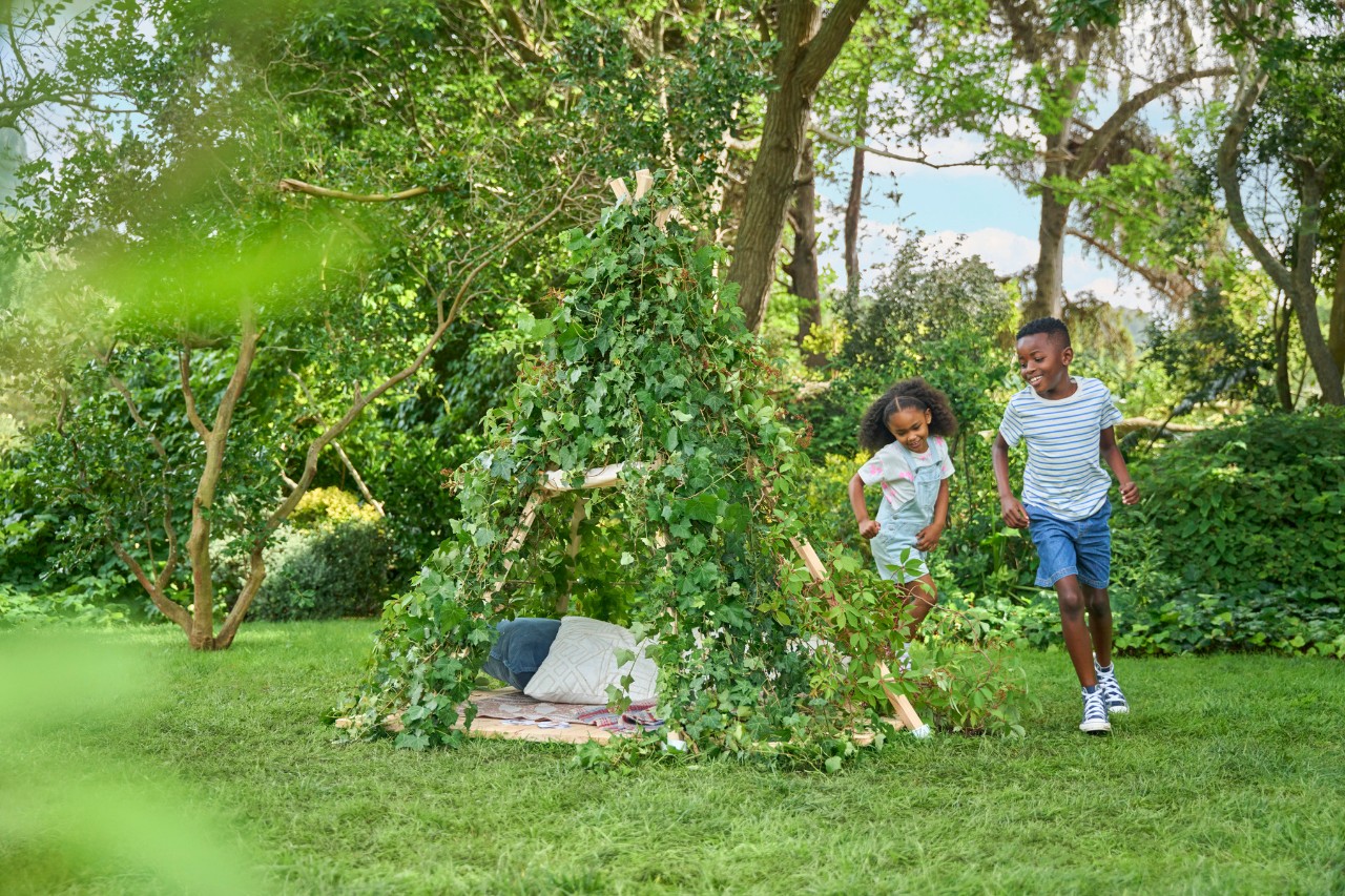 Children run around a natural garden play tent