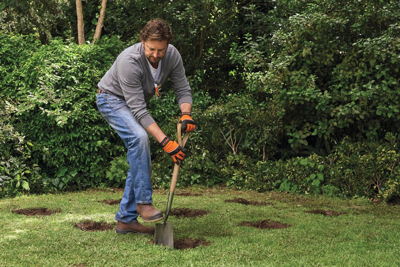 A man using a spade to dig 9 holes for pile foundations for a diy garden shed