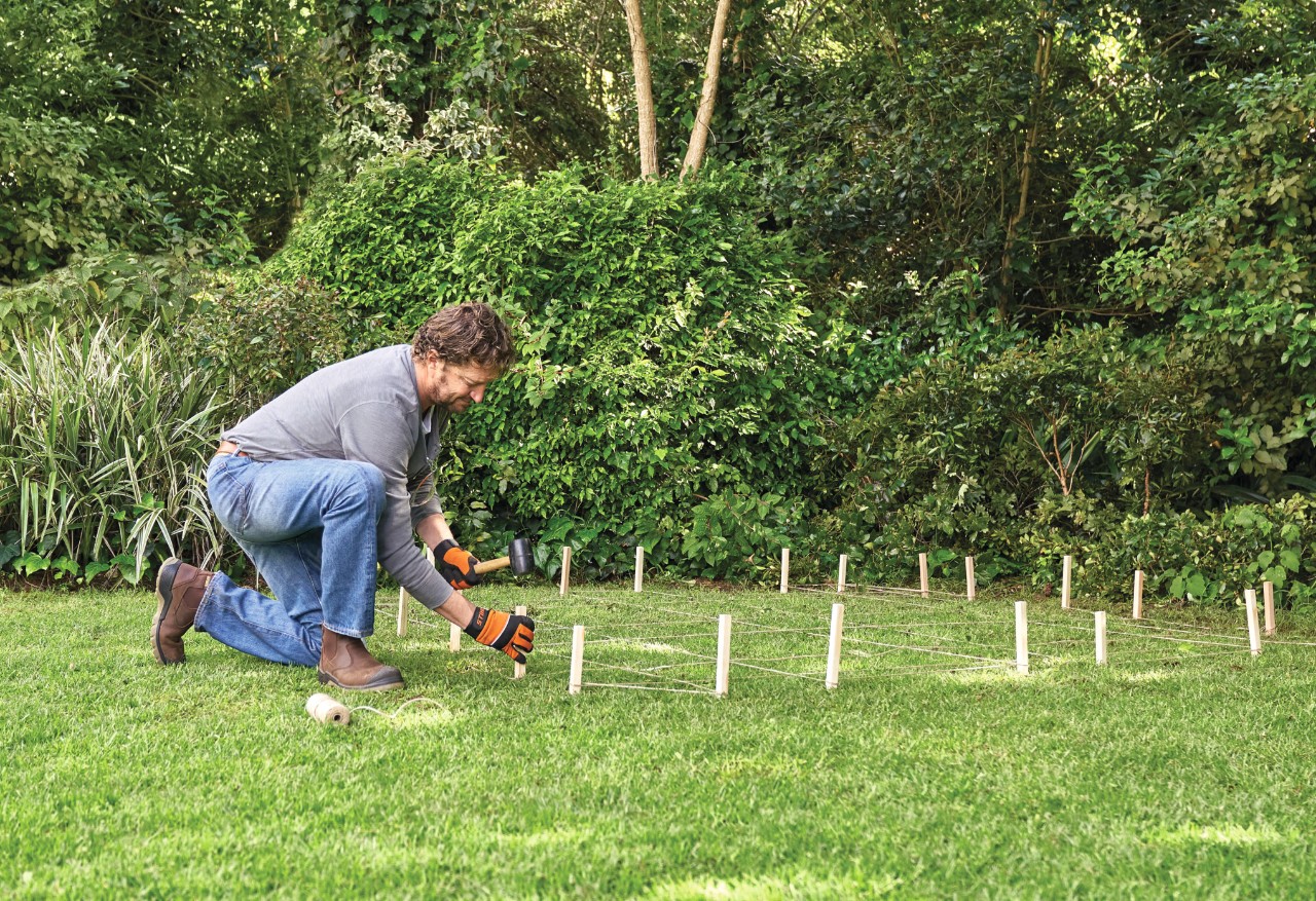 A man staking out a shed footprint on grass