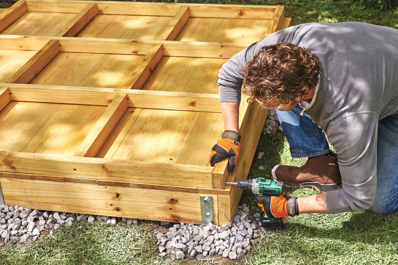 A man screws together a frame-and-panel wall for a garden shed