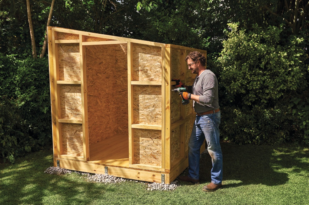 A man screwing together the assembled walls of a garden shed