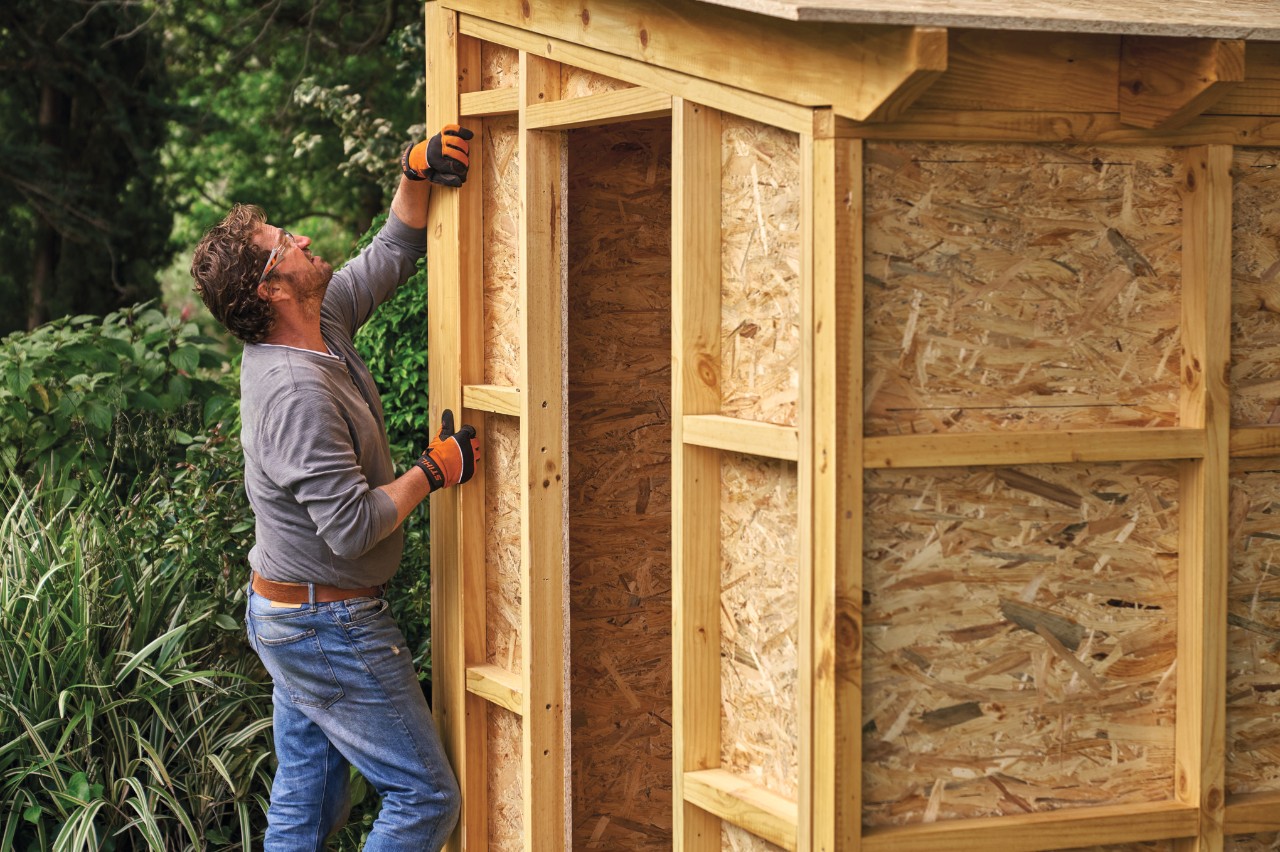 A man fixing a piece of timber cladding vertically in place on the outside of the garden shed frame