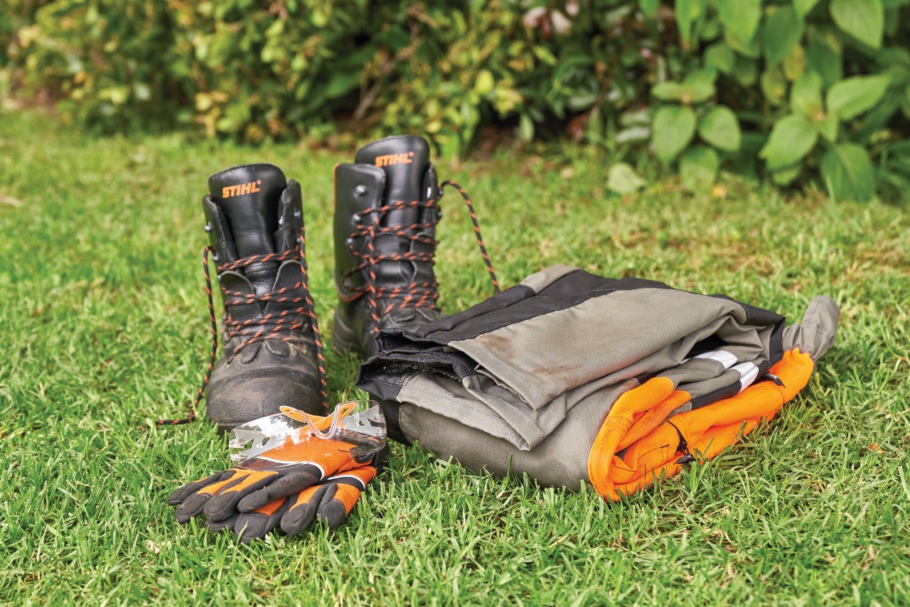 Boots, protective gloves and cut protection trousers laid out on grass