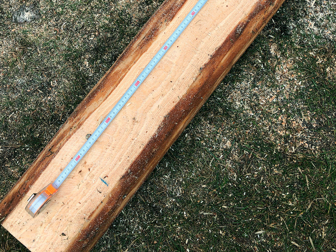 A folding rule lies on a piece of wood to mark the length of the boards for the table top