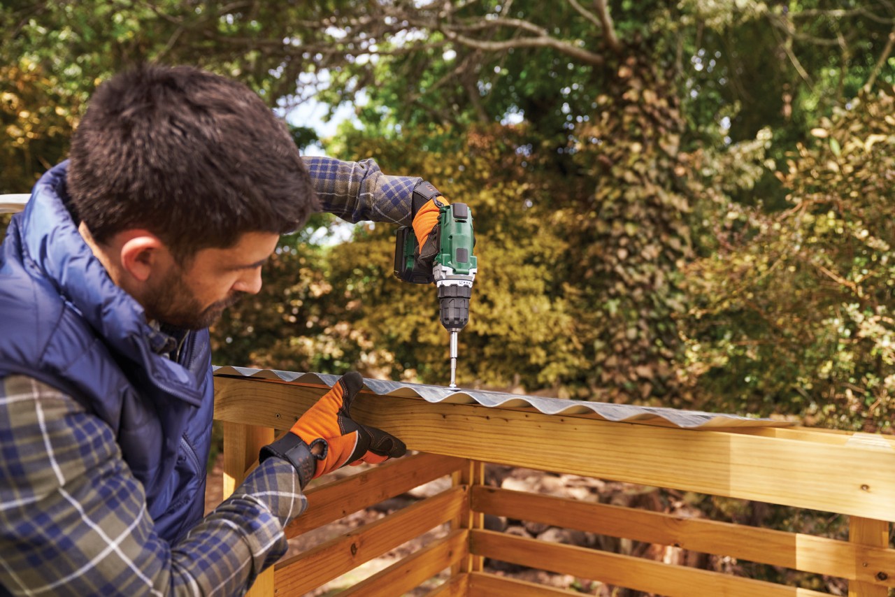 A man attaching corrugated sheet to a wooden log store