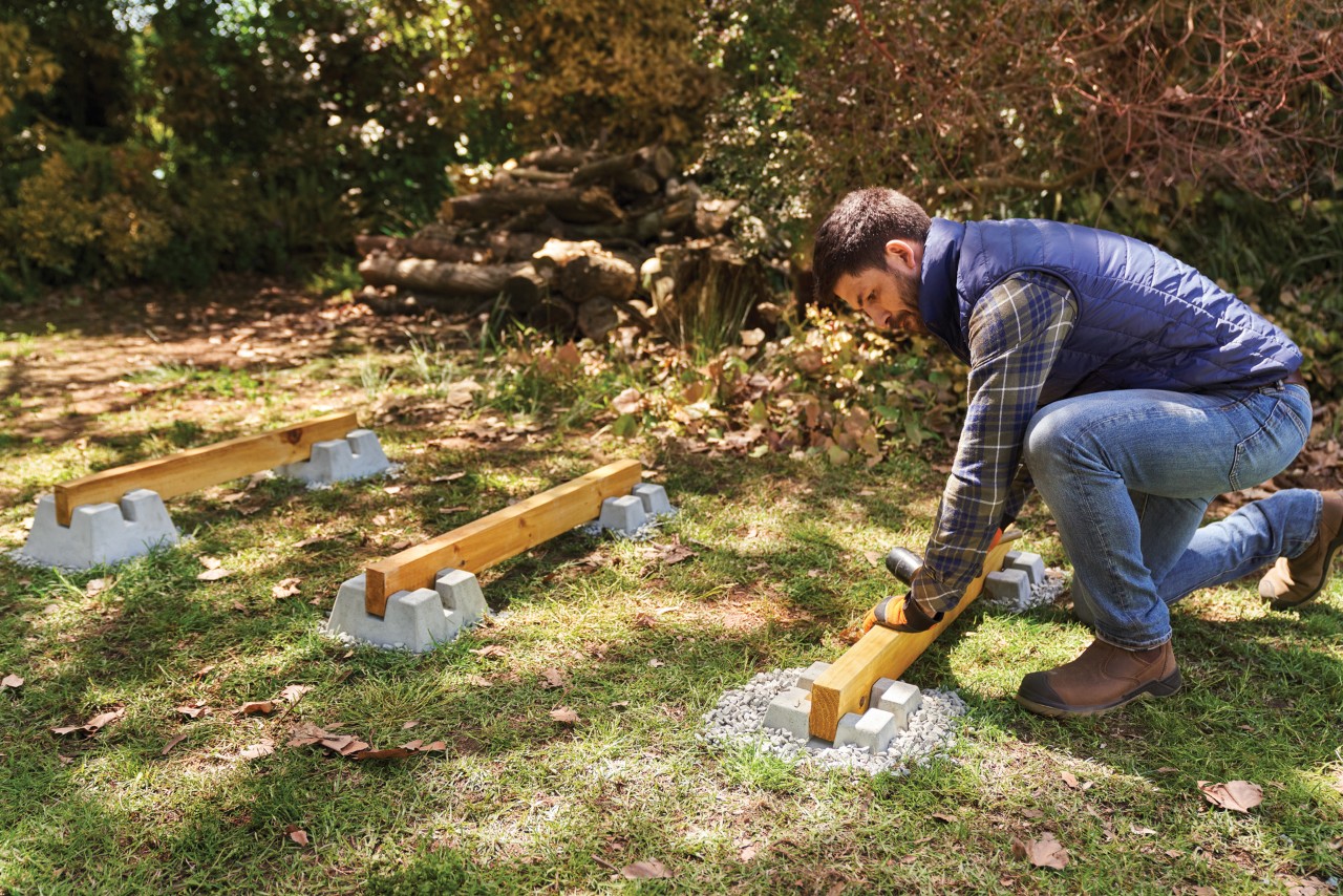 A man setting three wooden joists into a prepared foundation of decking blocks
