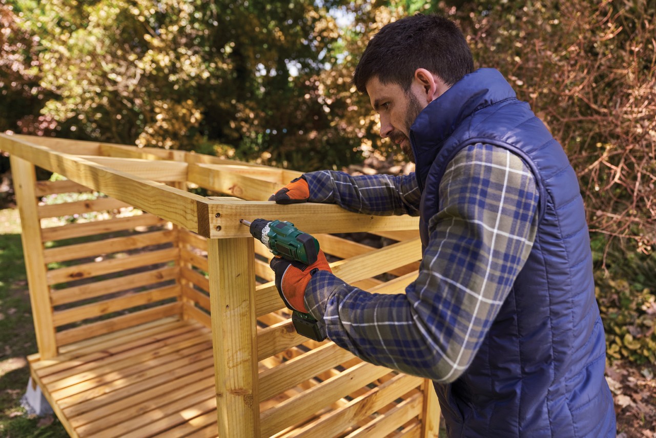 Man screws roof for a wooden log store
