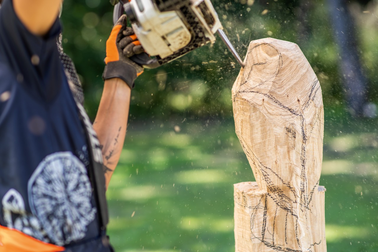 A roughly carved wooden owl has details added to its face by a woman using a STIHL chainsaw.