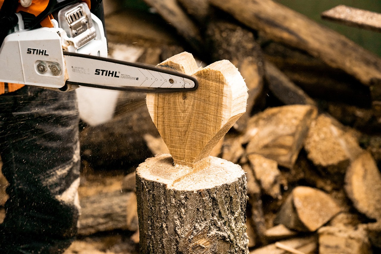 The edges of a standing wooden heart ornament being smoothed off with a STIHL 