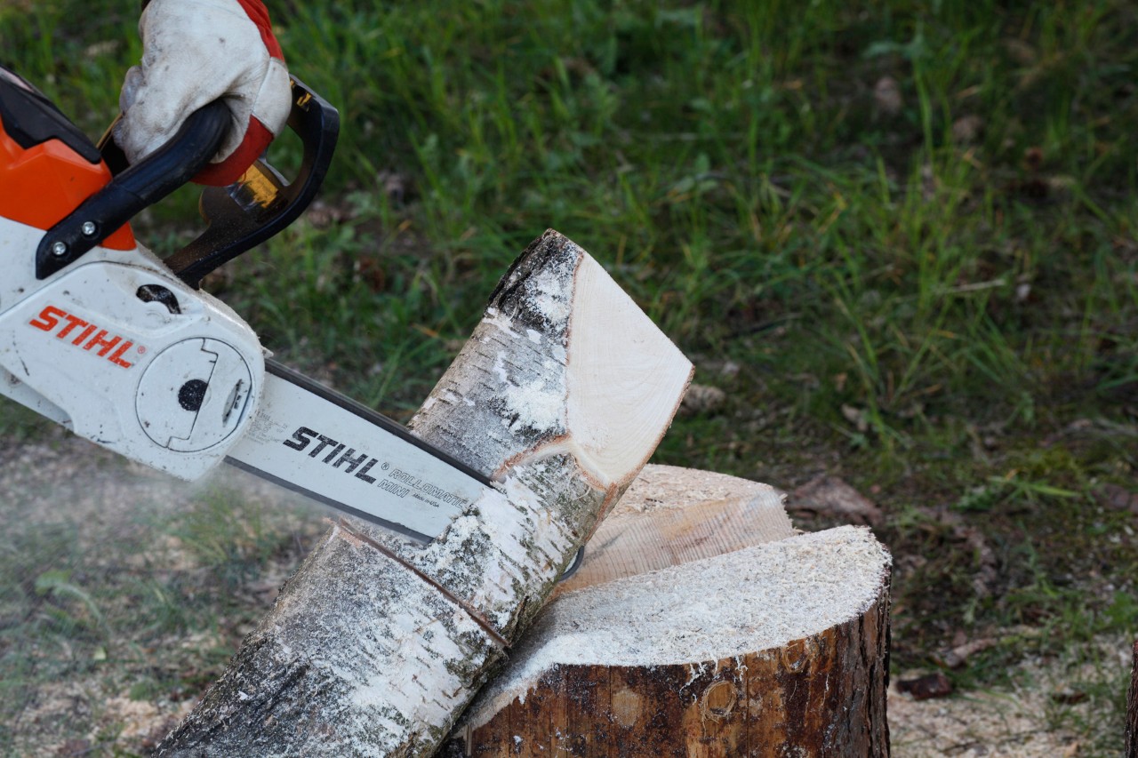 A STIHL MSA 140 C chainsaw being used to carve a flame shape into a log