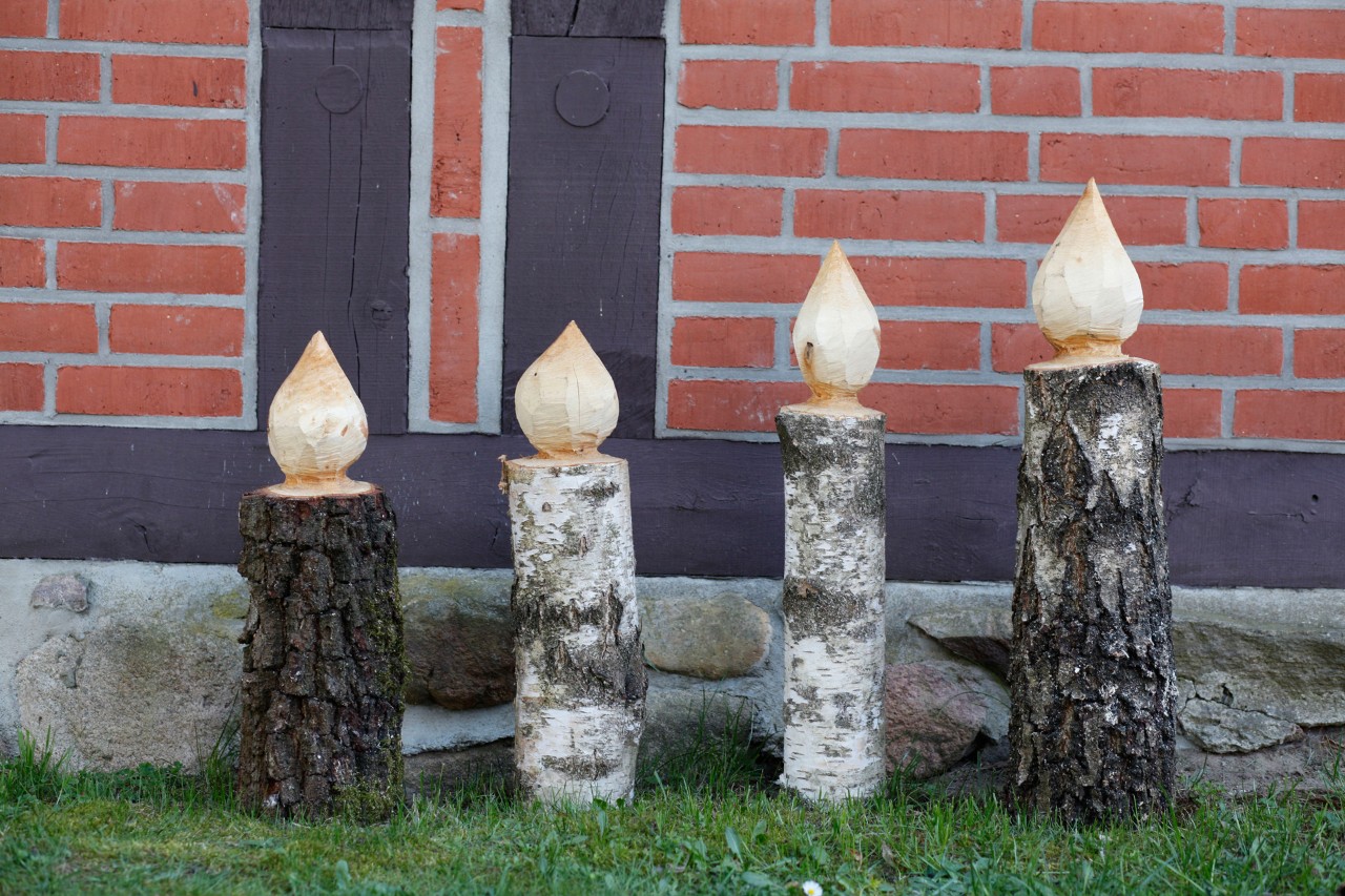 Four DIY wooden candlesticks standing on a lawn in front of a red brick wall