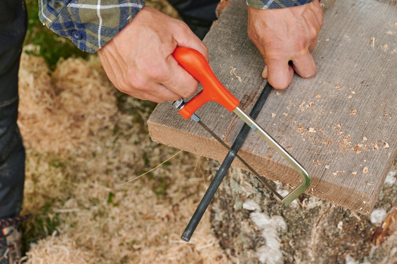 A metal stick being sawn to length with a hacksaw.