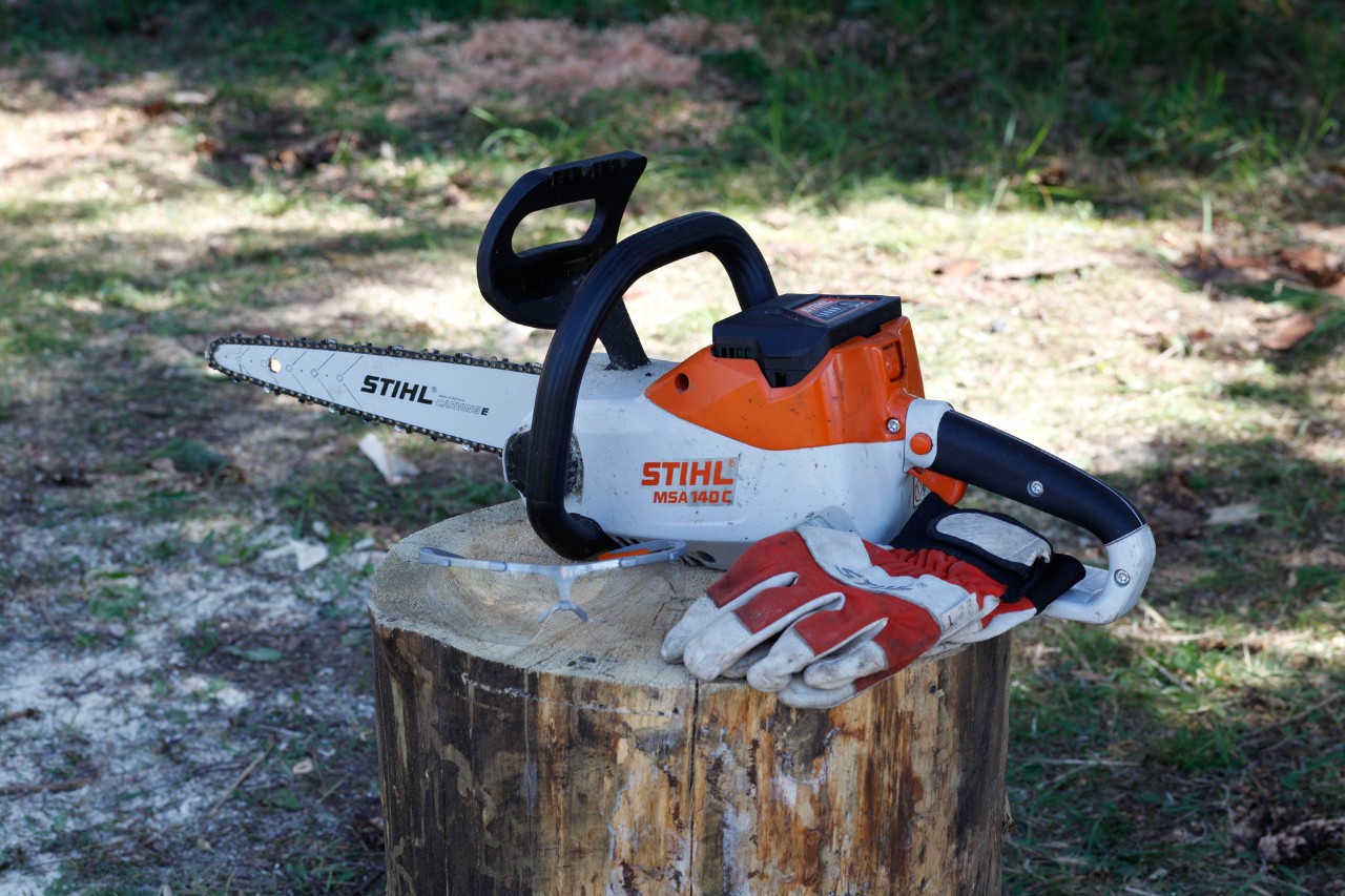 A STIHL MSA 140 C cordless chainsaw and protective gloves on a tree stump