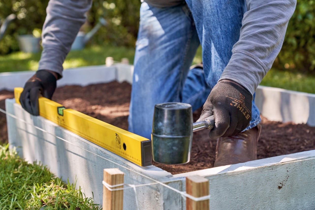 Build a raised bed from boards: edging stones being checked with a spirit level and hammered into place
