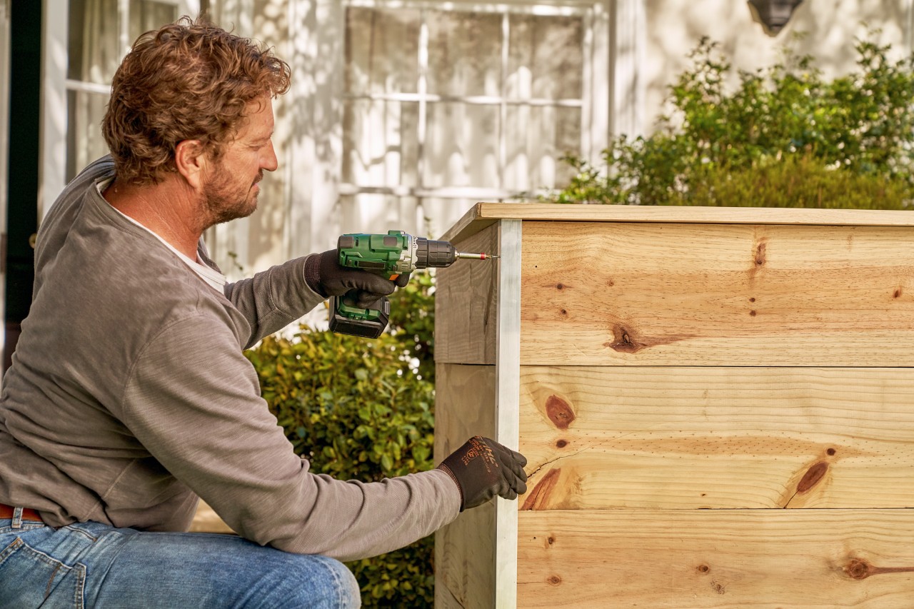 Build a raised bed from boards: a man screws aluminium angle to the outside edge of the raised bed