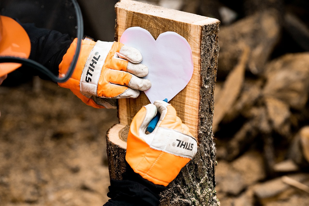 Make a wood heart ornament: a cardboard heart-shaped template on the flat wooden face being drawn around with chalk