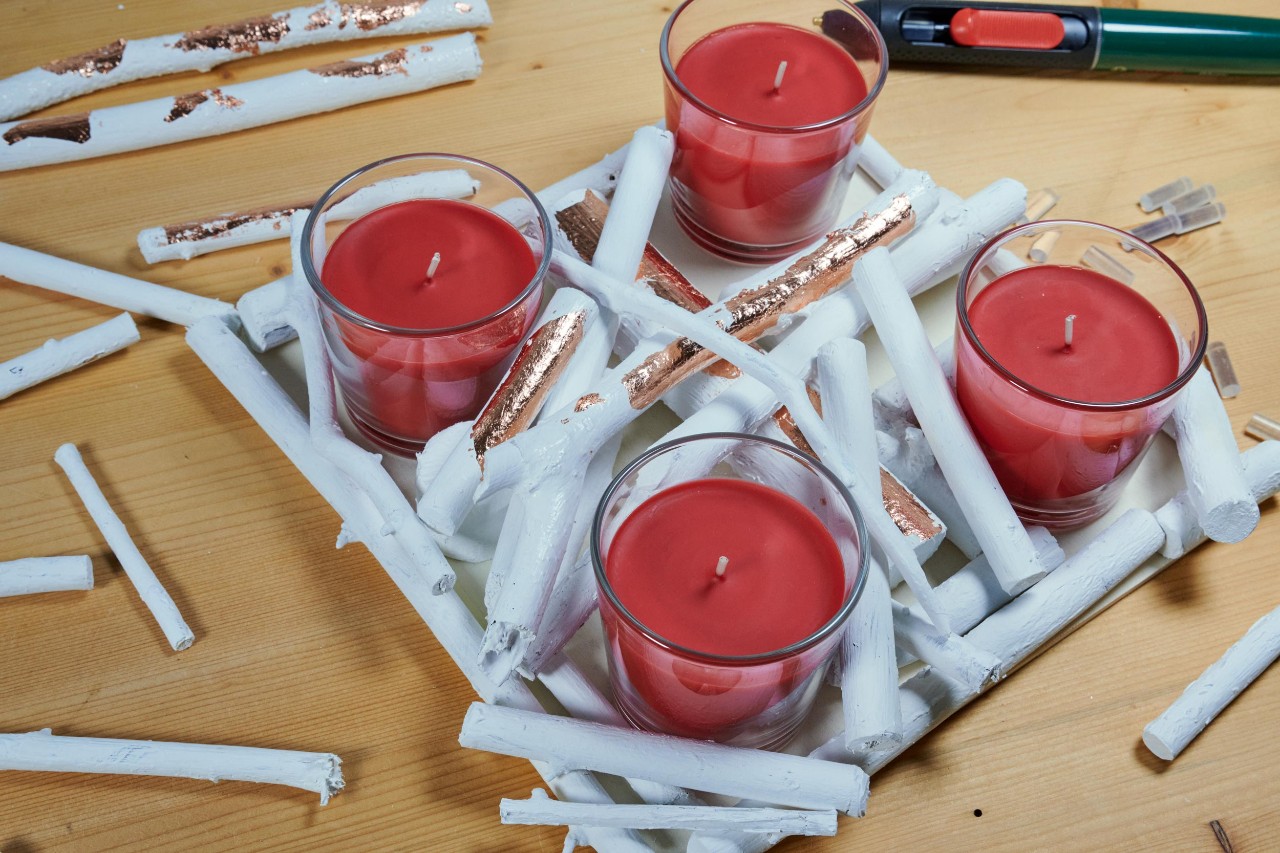 DIY advent wreath: white twigs being built up around the candle glasses on the board