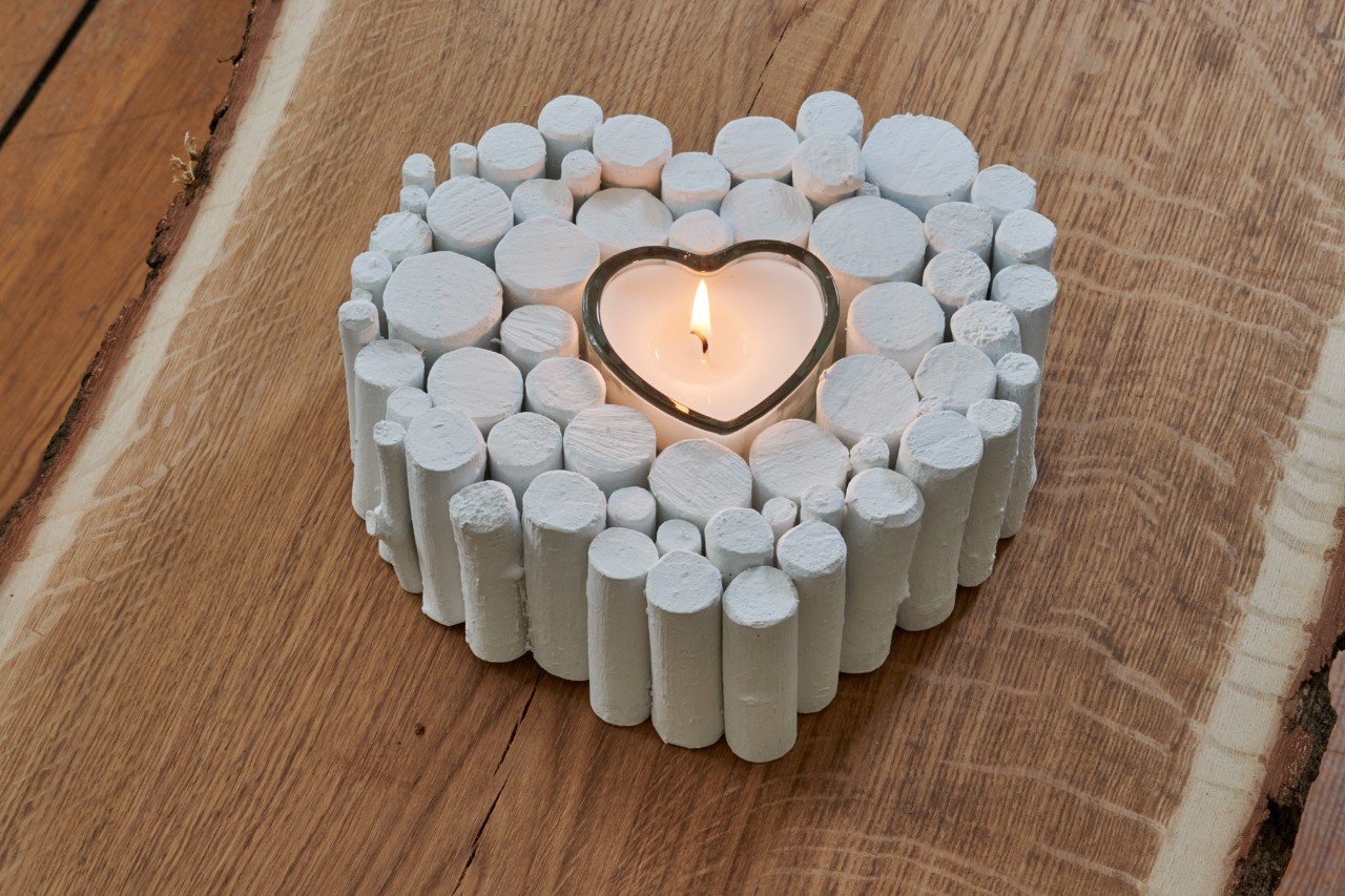 A finished DIY heart ornament made from a branch and painted white, with a lit candle inside