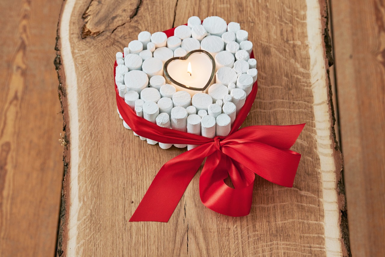 DIY branch heart: the finished decorative heart with a candle burning in it and a red ribbon tied in a bow around it