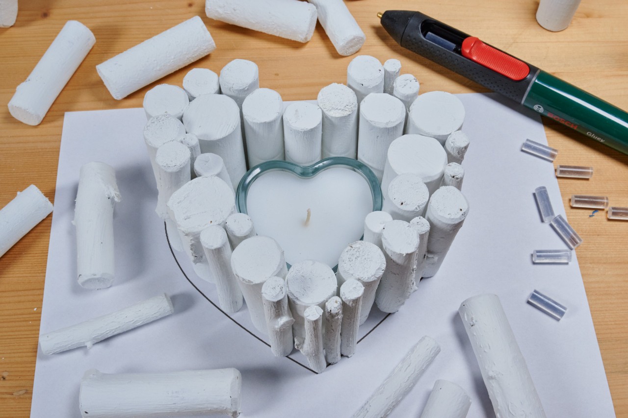 Upright painted branch pieces being glued together in a heart shape around a heart-shaped votive candle