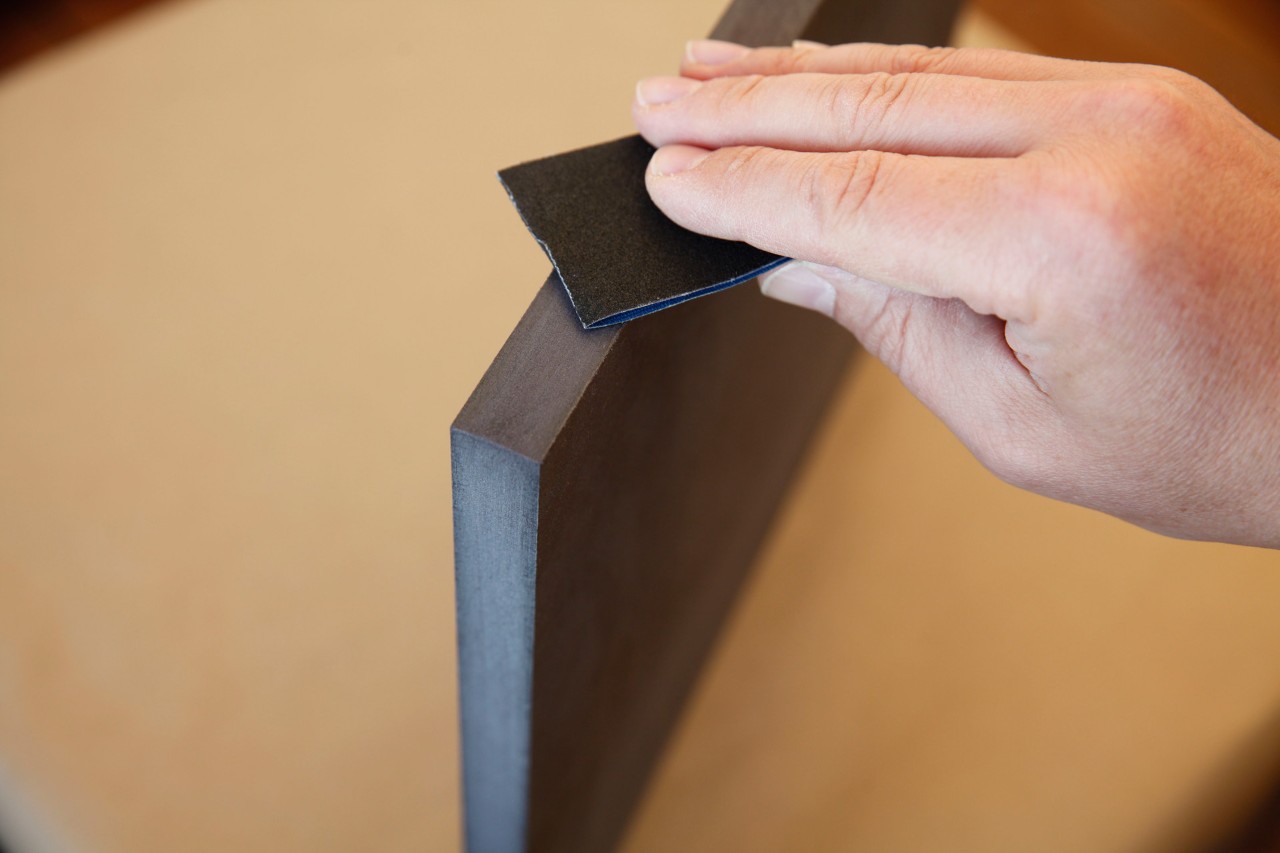 Close-up of the cut edge of an MDF board being sanded for a DIY log stool