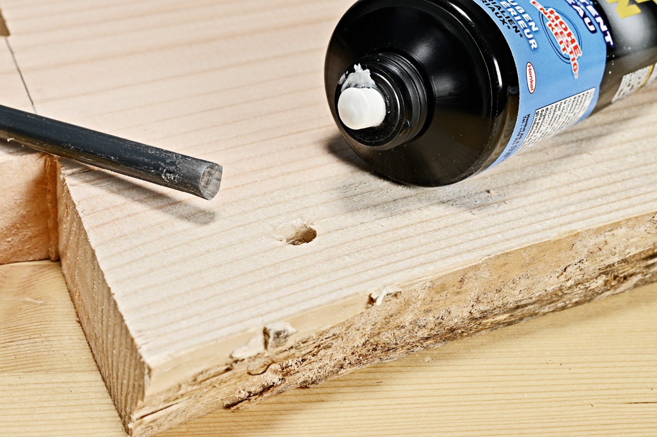 Construction adhesive and a metal rod beside a drilled hole in the wooden plank for the DIY side table