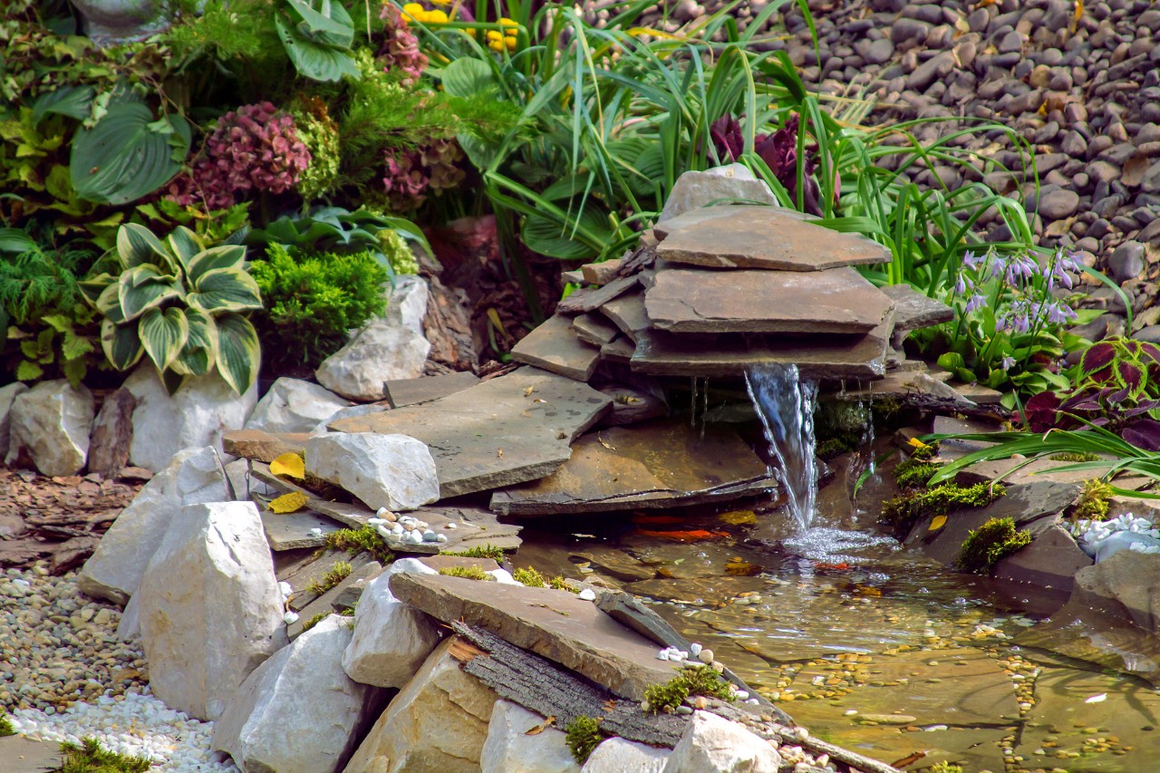Fountain at a small pond in a wildlife-friendly garden, decorated with plants, stones and slates