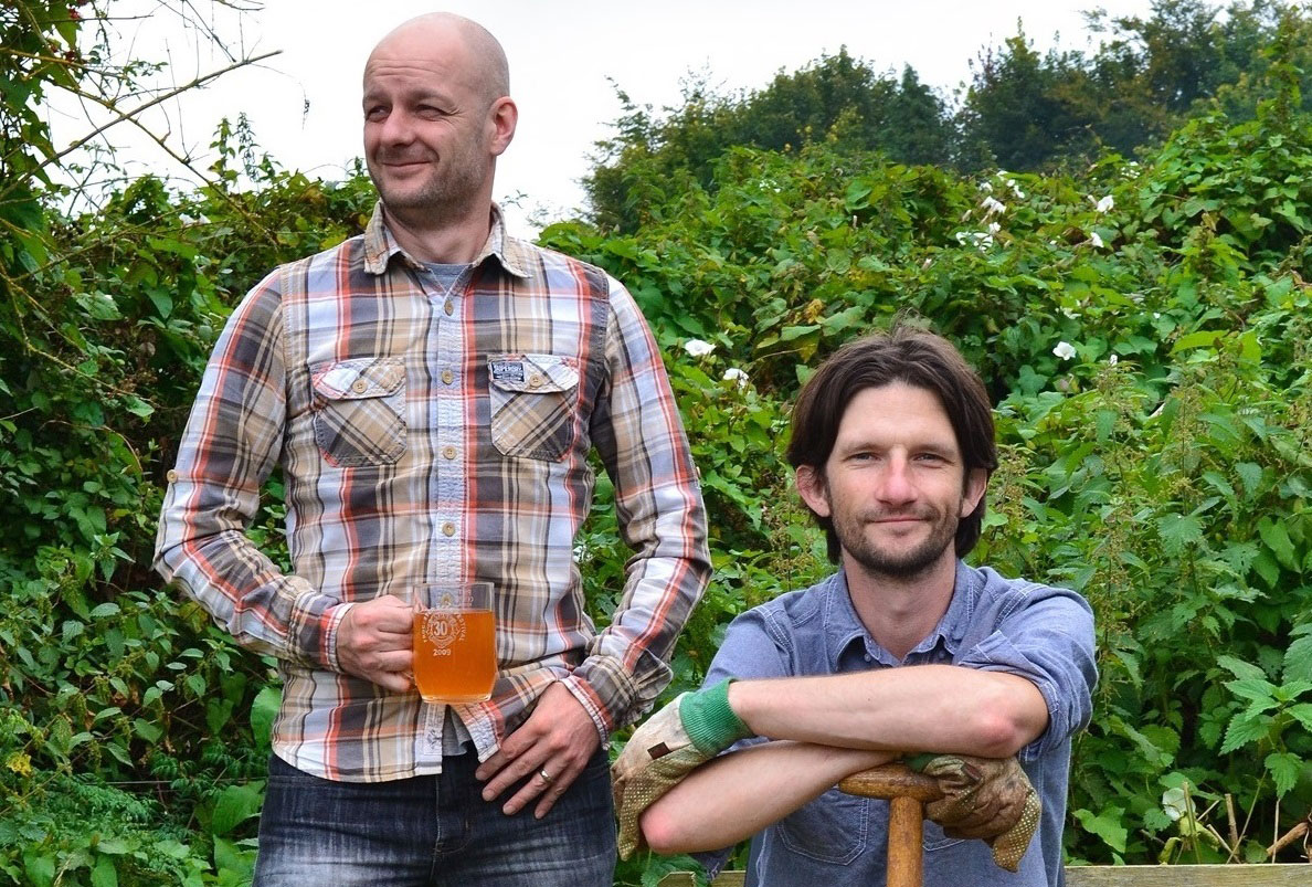 The two thirsty gardeners in a garden drinking tea and sittin on a bench with a garden fork