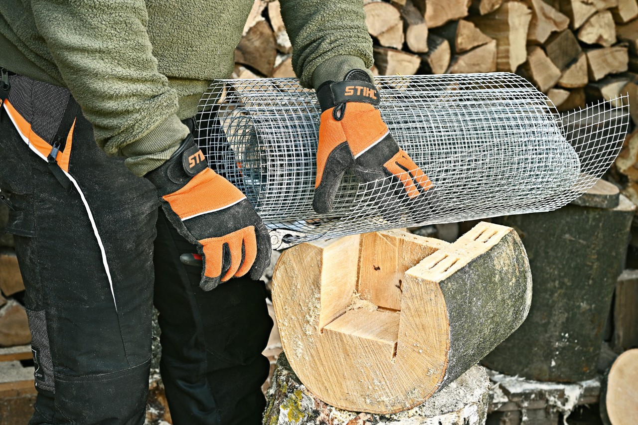 A person wearing protective gloves cuts wire mesh