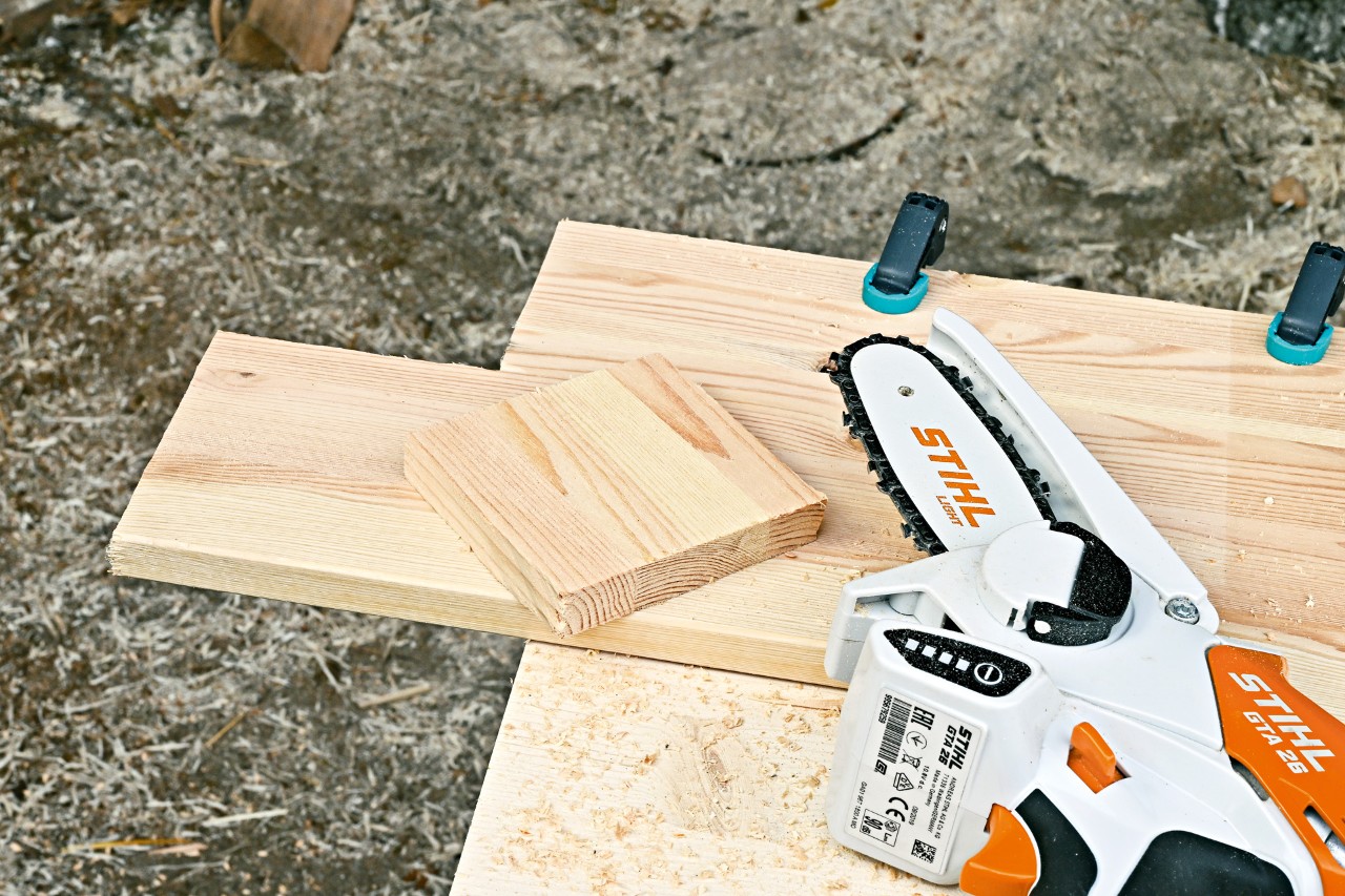STIHL GTA 26 cordless garden pruner next to a piece of wood from which a square has been cut 