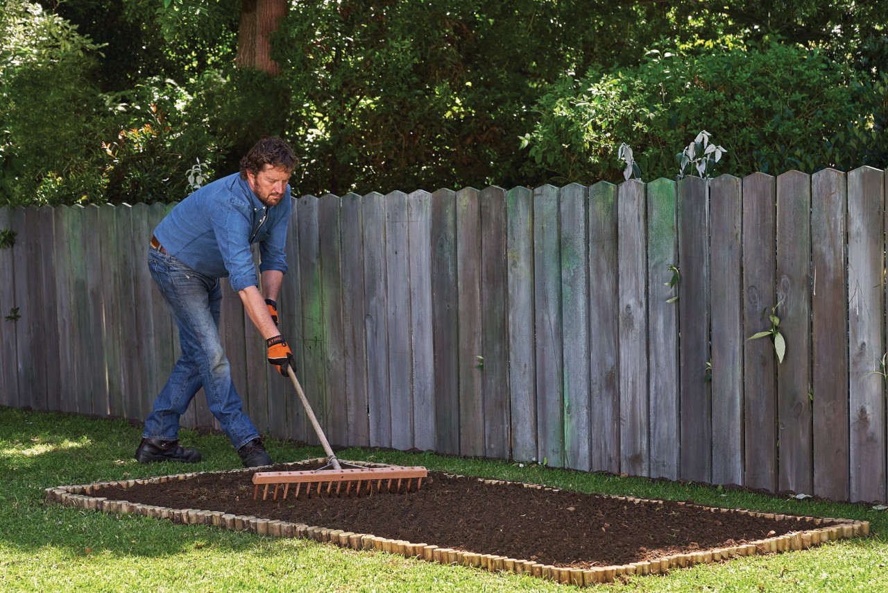 Person levelling off soil with a rake to build a plant bed