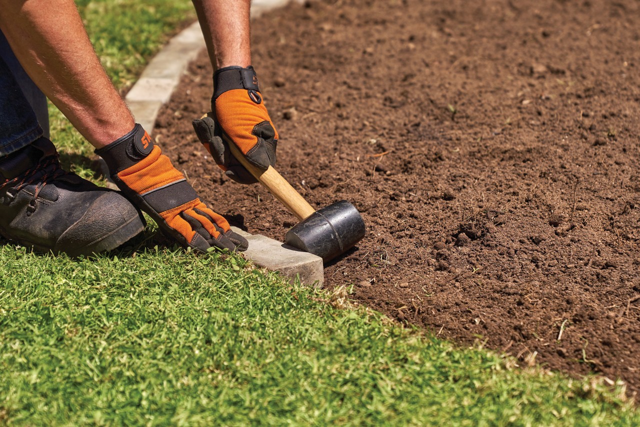A man hammering in stones along a lawn edge to make a DIY garden edging