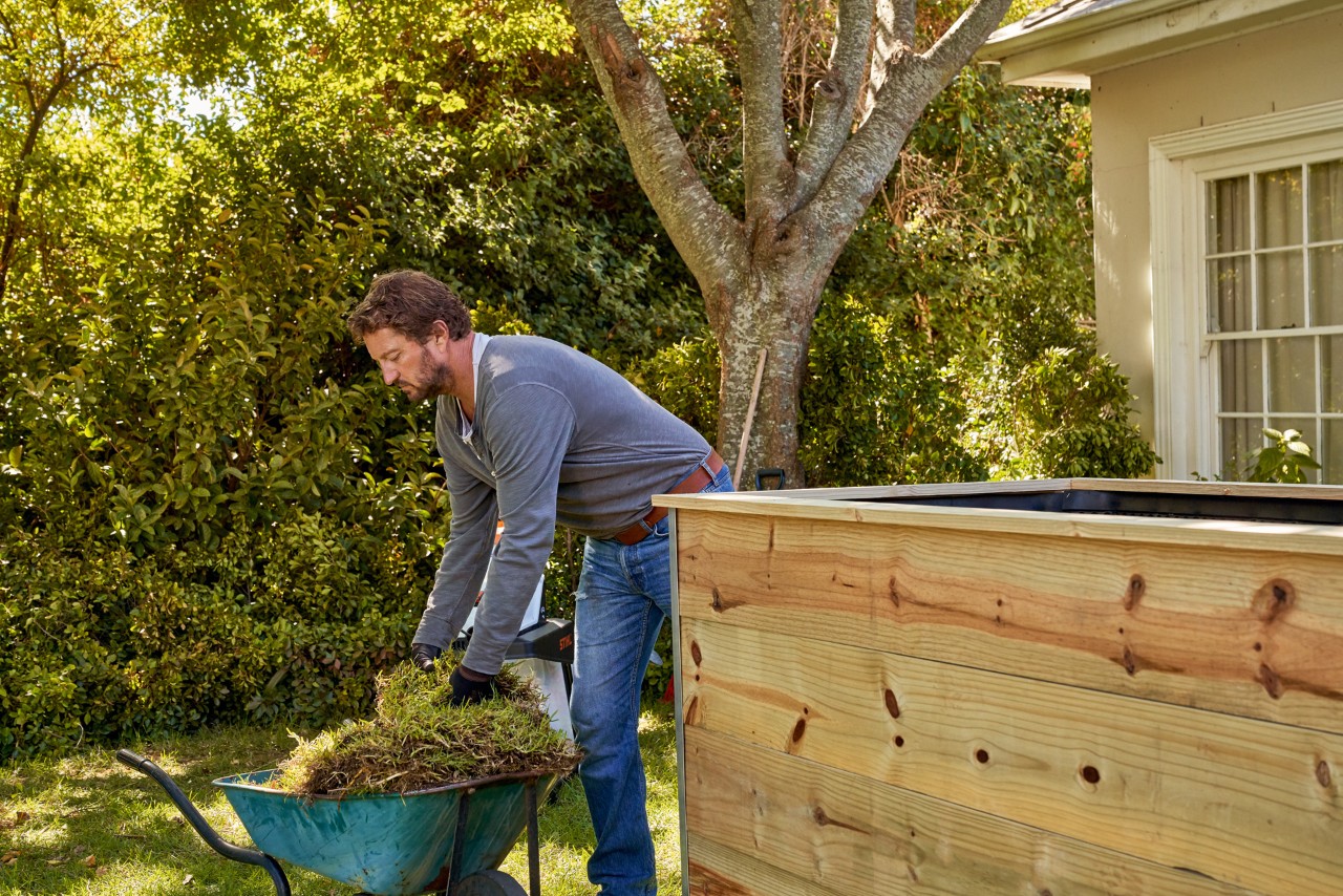 A man lifting pieces of turf out of a wheelbarrow into a raised bed