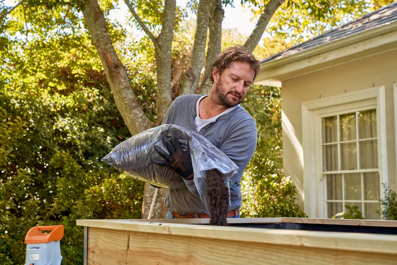 A man emptying soil from a plastic sack into a raised bed