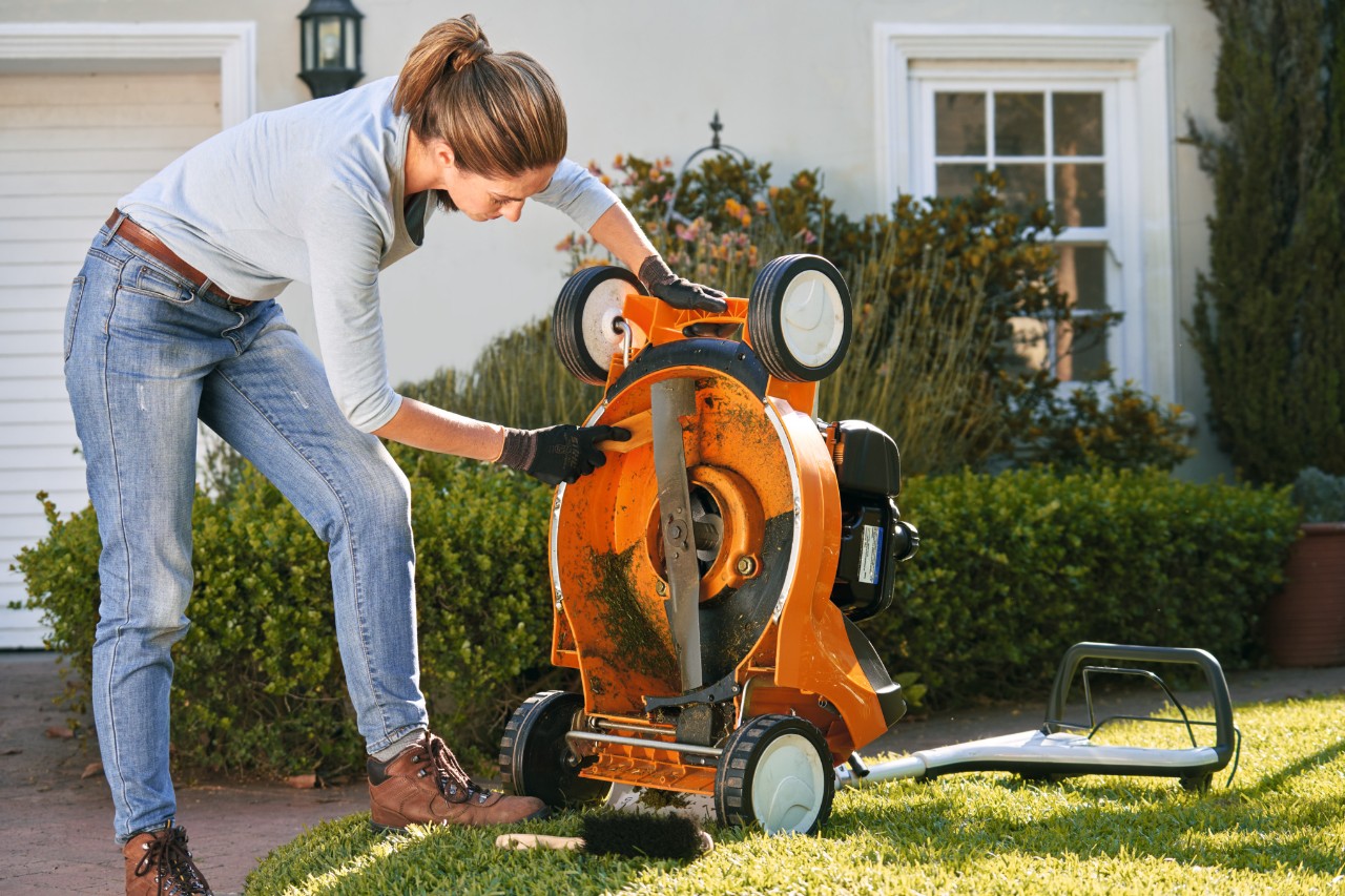 woman brushing underside of STIHL lawn mower clean of grass