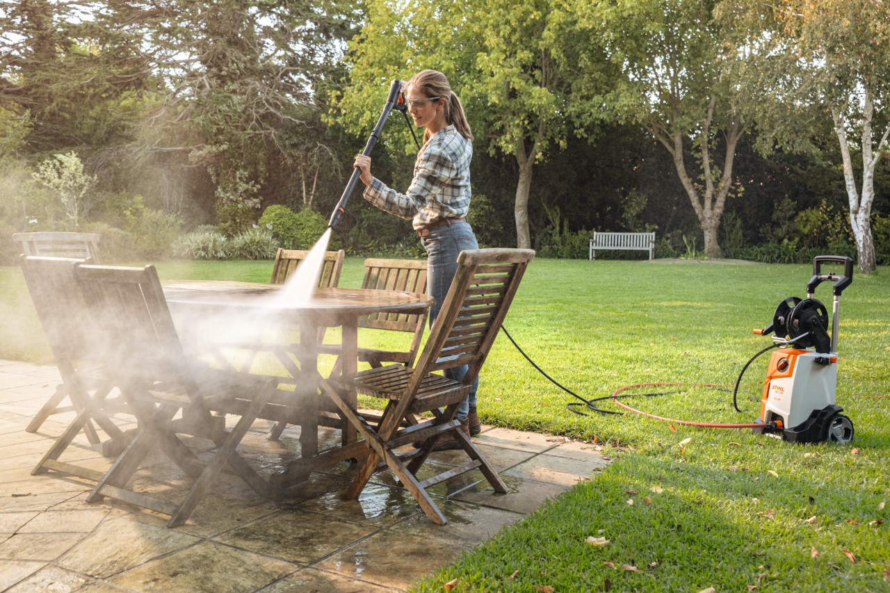 Woman cleaning table set on patio with STIHL RE 130 pressure washer