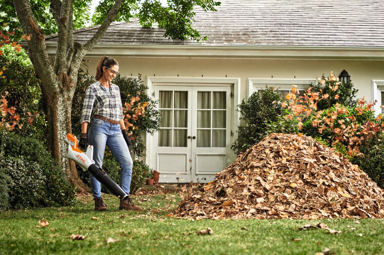 Woman blowing autumn leaves off path with STIHL BGA 30 leaf blower