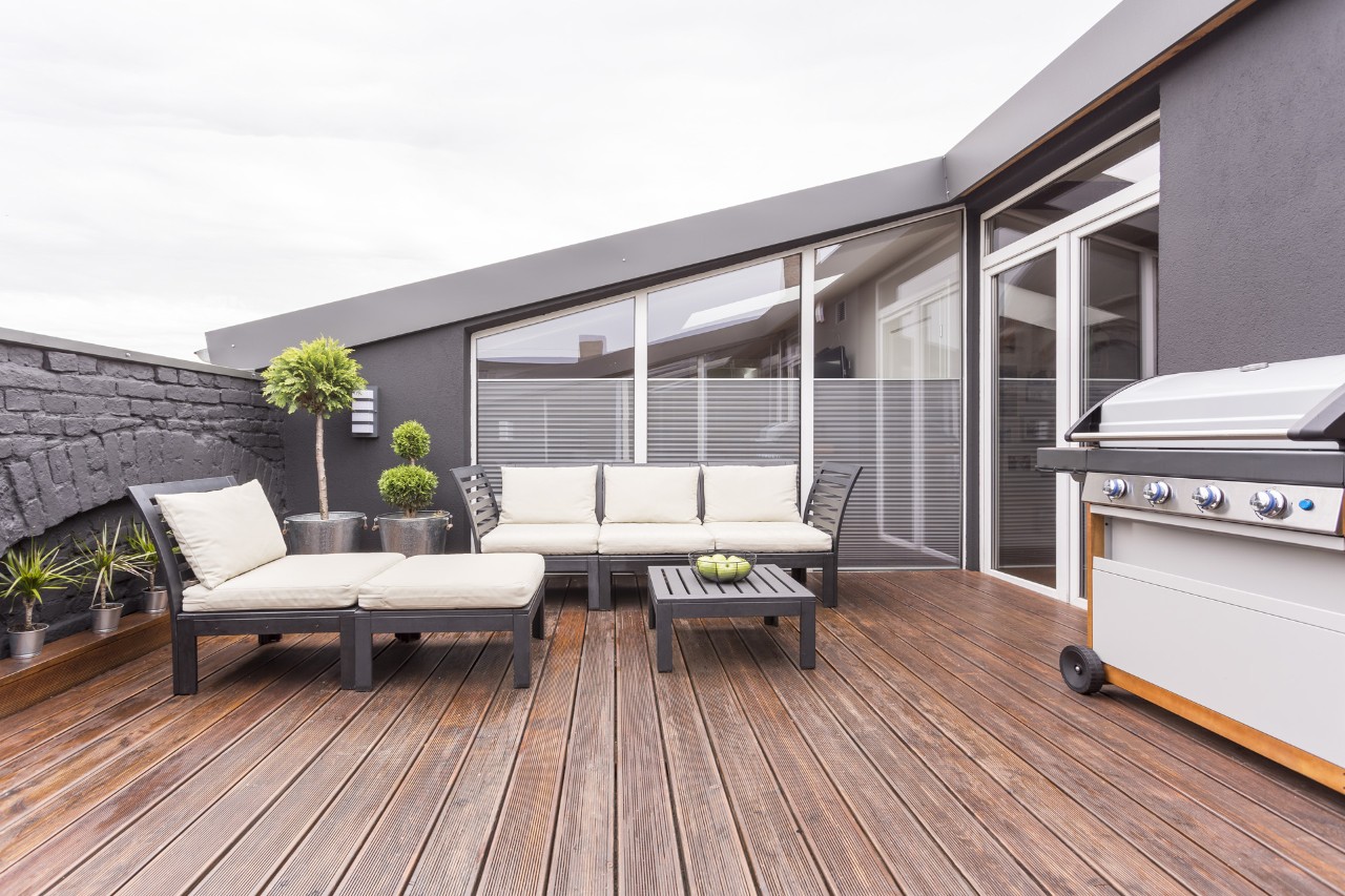 A roof terrace furnished with sofa, lounger, barbecue and wooden flooring