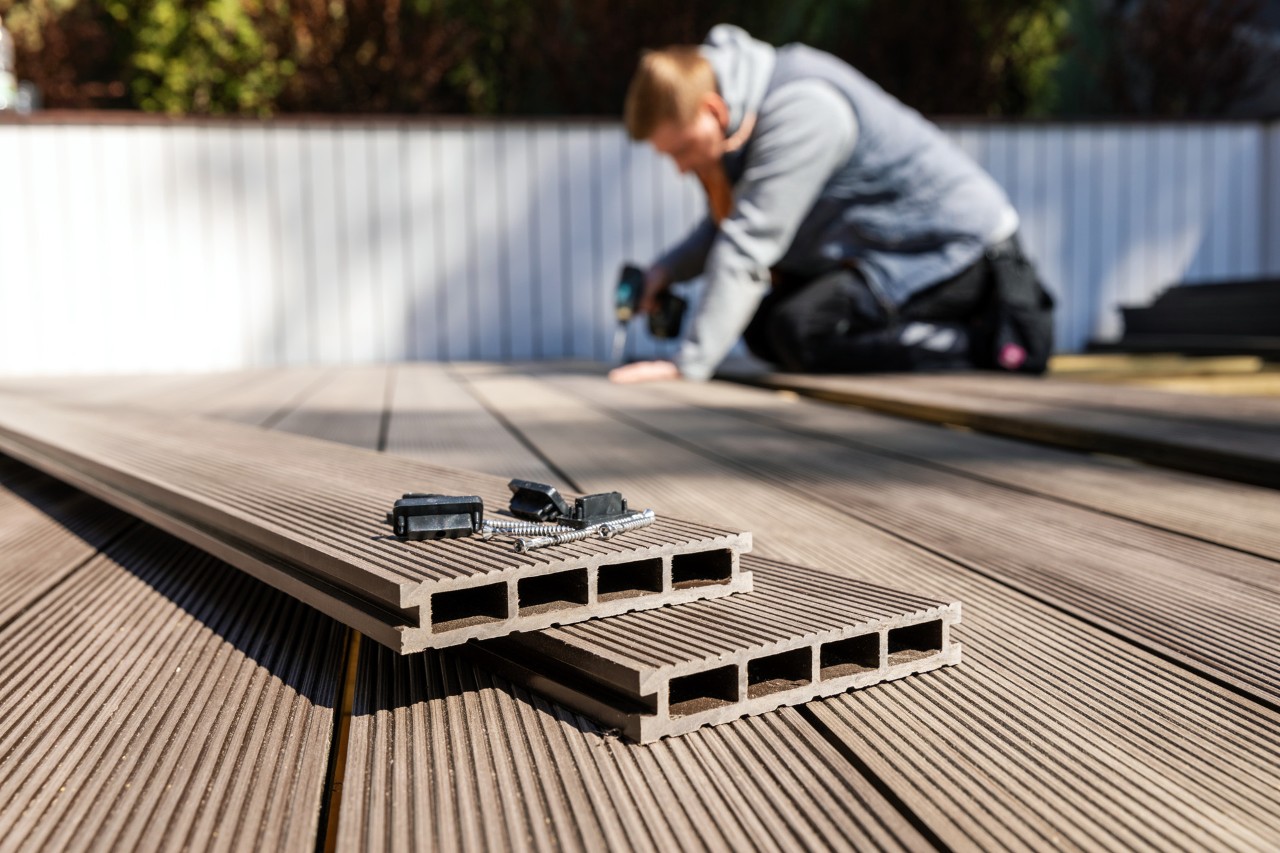 A man laying a WPC floor beside a white fence