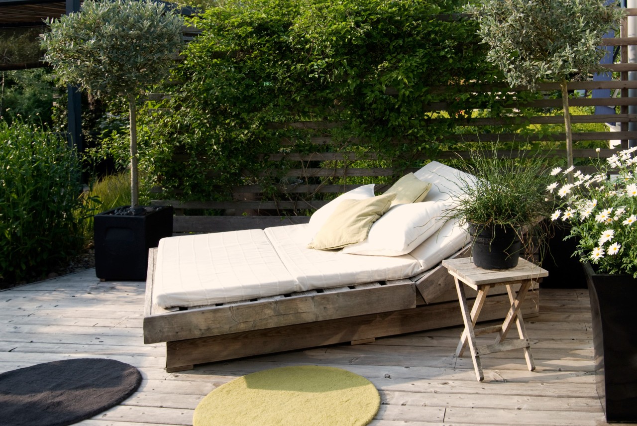Oasis, relaxation area, outdoor lounger in a small garden with plant tubs all around and a privacy screen.