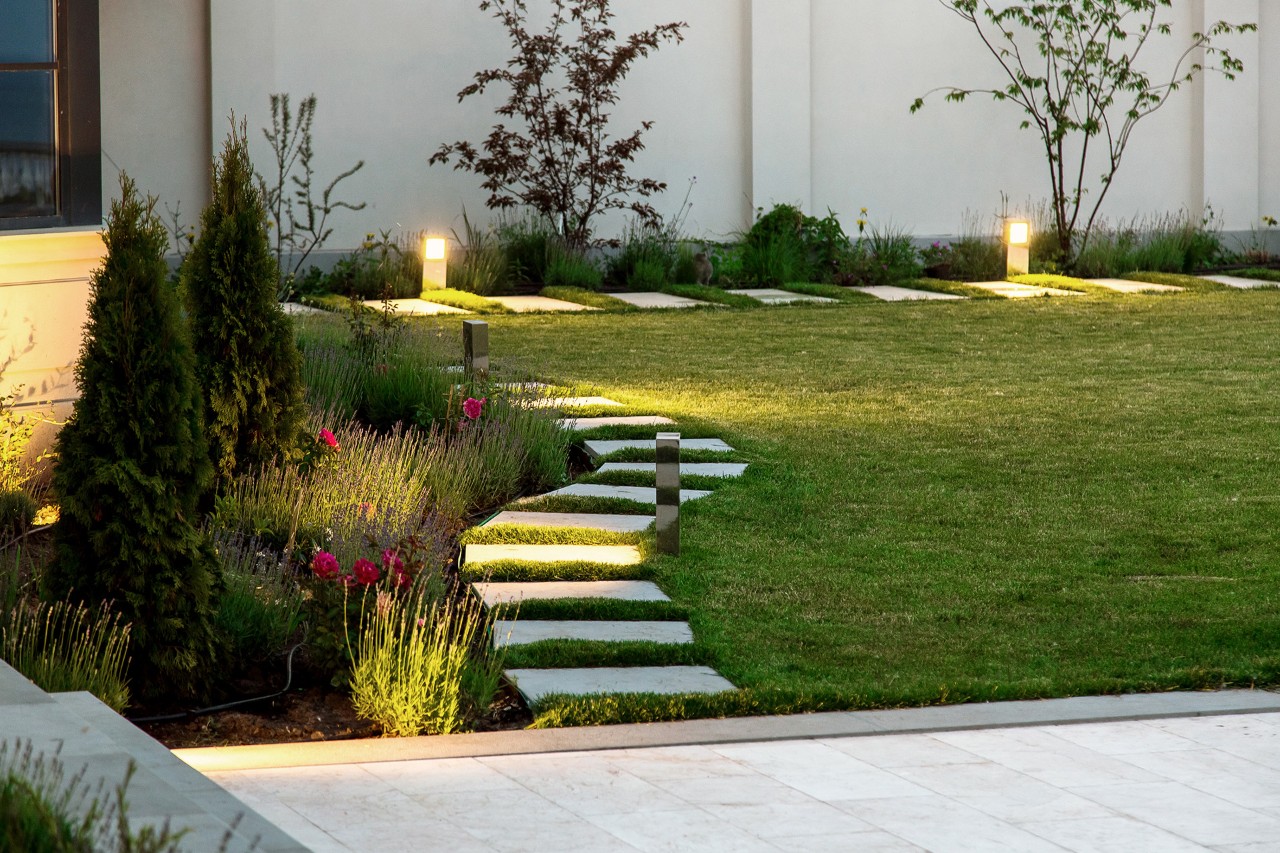 Small garden in the evening, flower bed, green lawn, marble-effect path made of square slabs, decorative solar lighting.