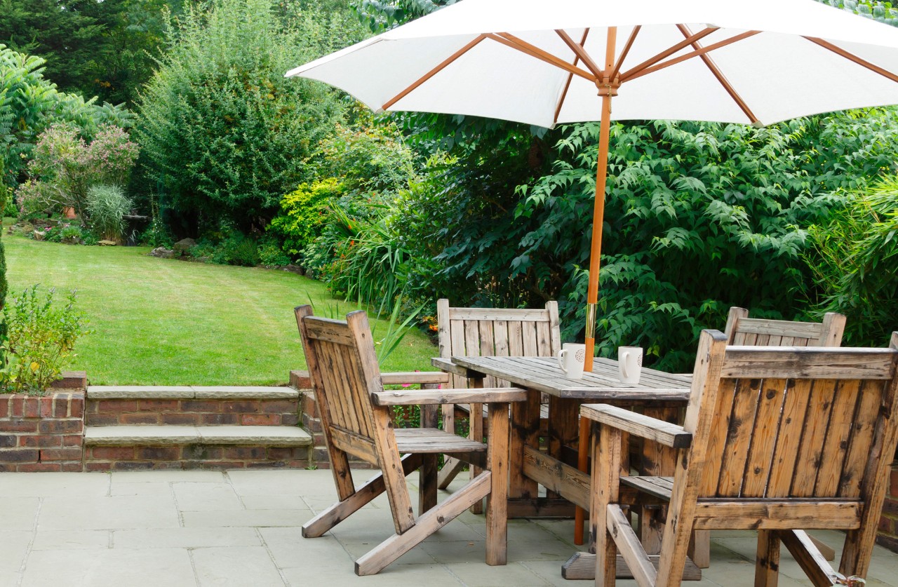 A sunken garden in a small garden with paving stones, garden furniture at the front and a lawn at the back.