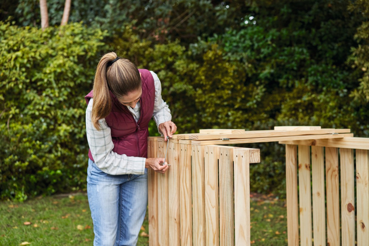Woman attaching cabin hooks to a DIY compost bin on a garden plot 