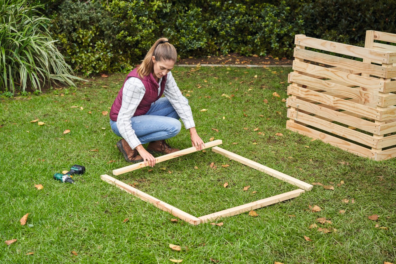 A woman placing slats for the composter frame at right angles to each other on a lawn 