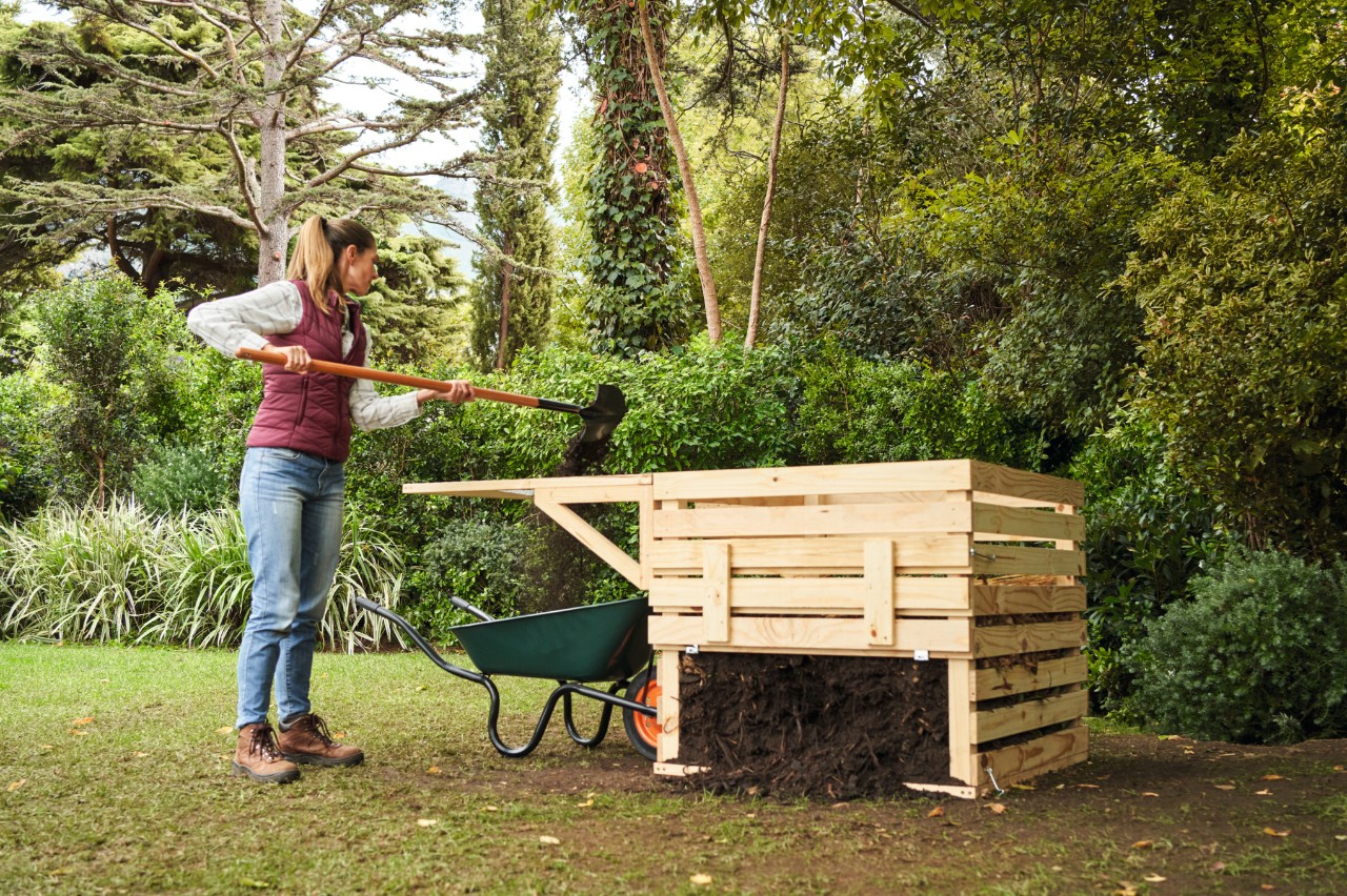 A woman on a garden plot sieving raw compost next to a DIY wooden compost bin